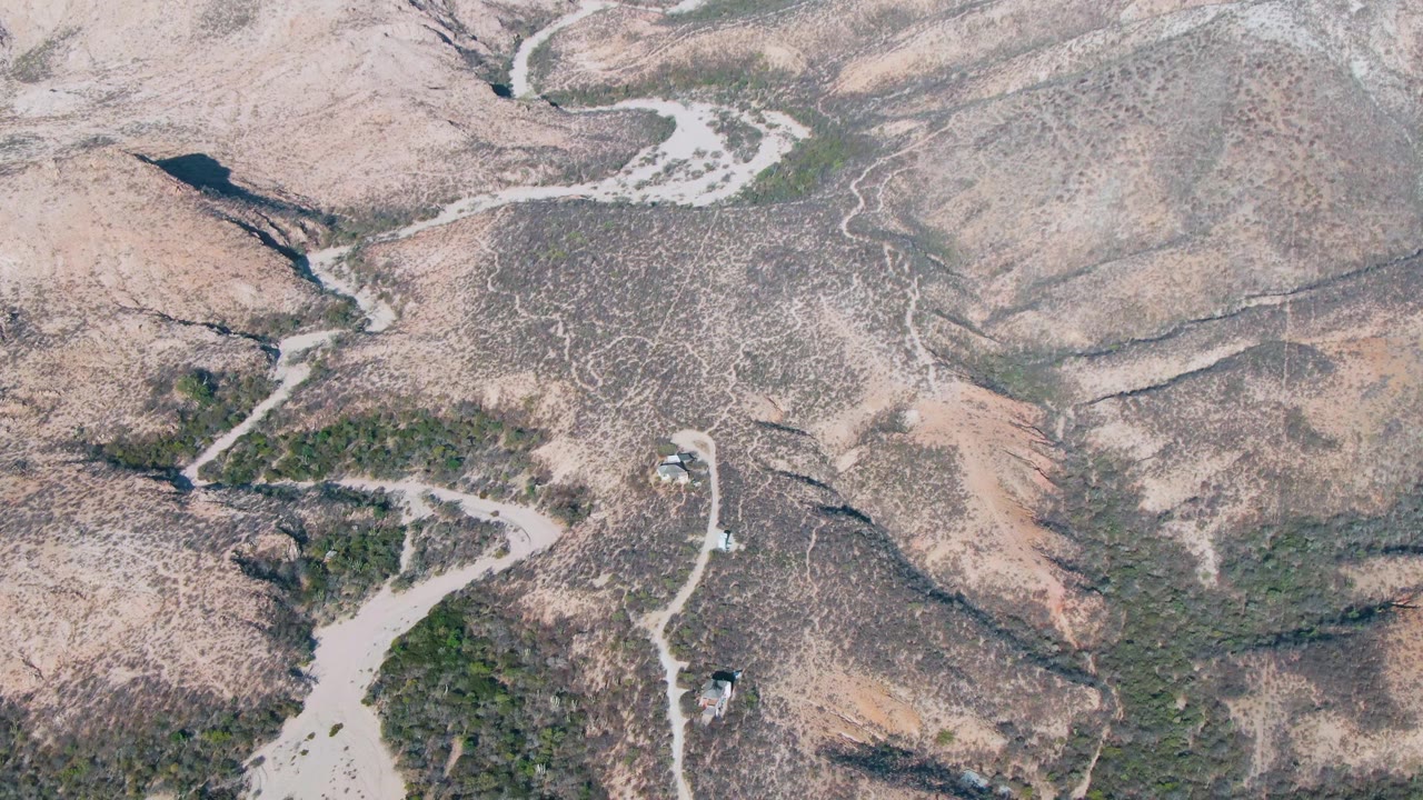 Aerial view in Cabo Pulmo, Baja California Sur with the vehicles slightly farther along the winding dirt route between scrub patches and dry hill slopes, with no visible people.