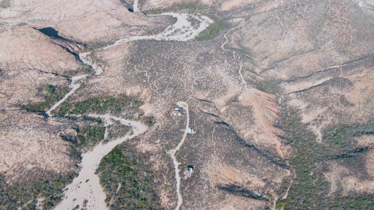 Drone-style overhead frame from Cabo Pulmo, Baja California Sur showing small vehicles on branching dirt tracks amid pale rocky hills and scattered vegetation, with no visible people.