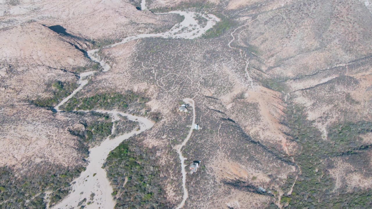 Aerial view of pale rocky hills crossed by dry riverbeds and sparse vegetation.
