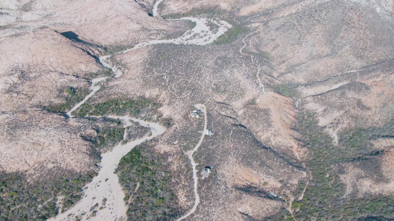 Aerial view in Cabo Pulmo showing a central winding dry wash, mottled rocky slopes, sparse green vegetation, and no visible people.