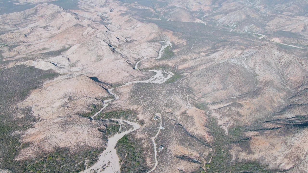 Aerial view of arid hills crossed by a pale winding riverbed.