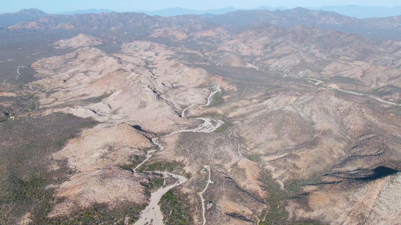 Aerial frame over Cabo Pulmo scrubby hills, with a pale dry channel running through the lower valley and no visible people.