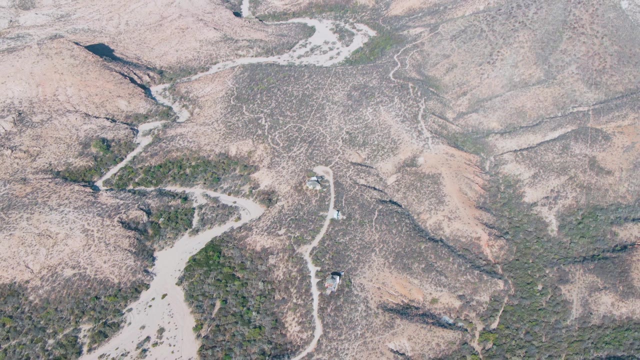 Aerial view of arid hills with a winding dirt road and sparse green vegetation.