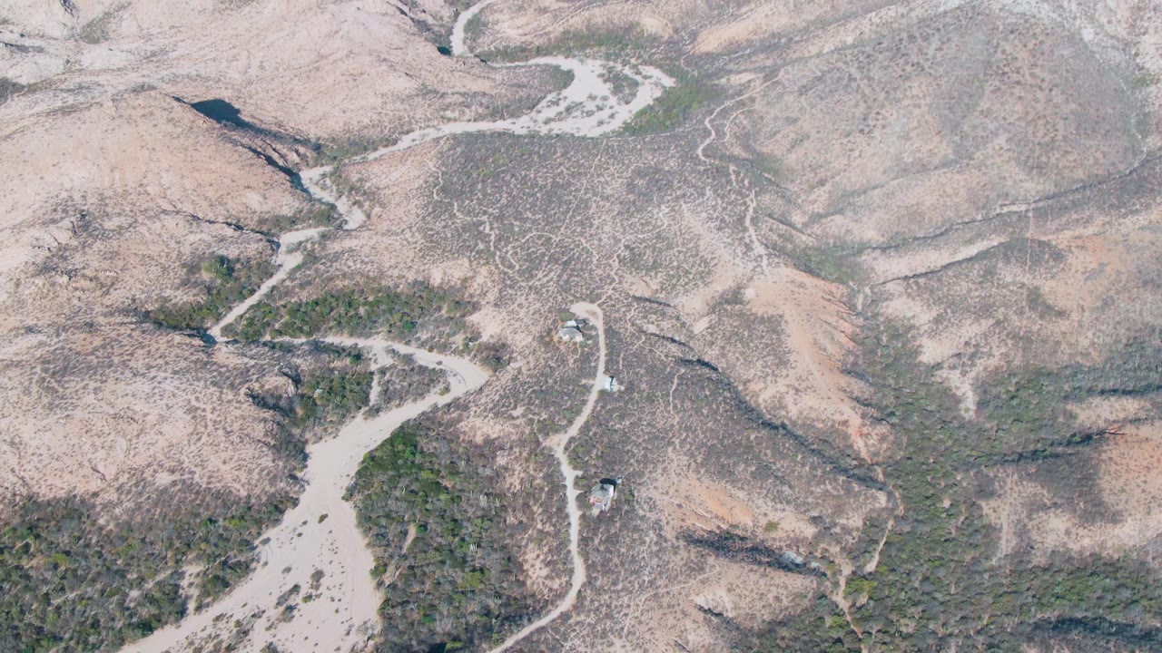 Overhead view in Cabo Pulmo showing a small vehicle on a pale dirt road between rocky dry slopes, with no visible people.