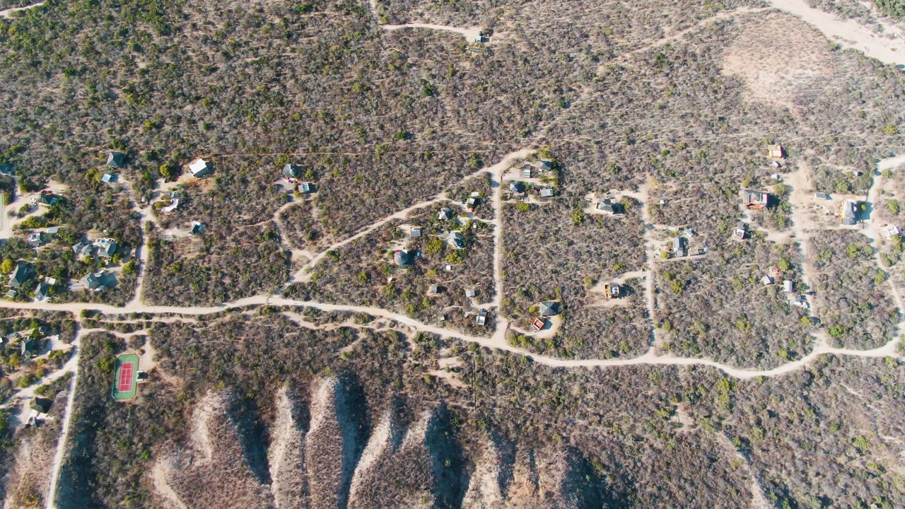 Drone view of a hillside neighborhood crossed by pale dirt roads.