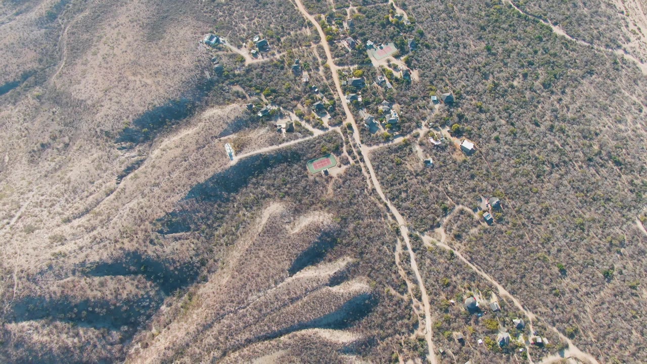 Aerial frame over dry hilly terrain near Cabo Pulmo, Baja California Sur, with winding dirt roads, scattered homes, sparse vegetation, and no visible people.