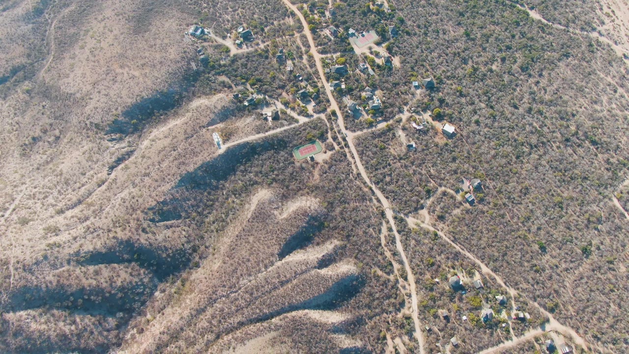 Aerial view in Cabo Pulmo showing pale ridgelines, scrub-covered slopes, unpaved roads, several small homes, and no visible people.