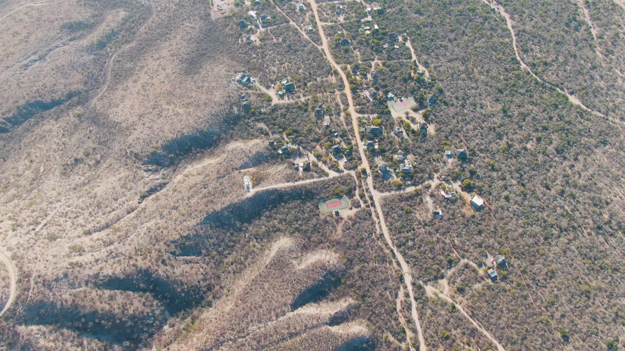 Drone view of scrub hills with a central dirt road and small houses