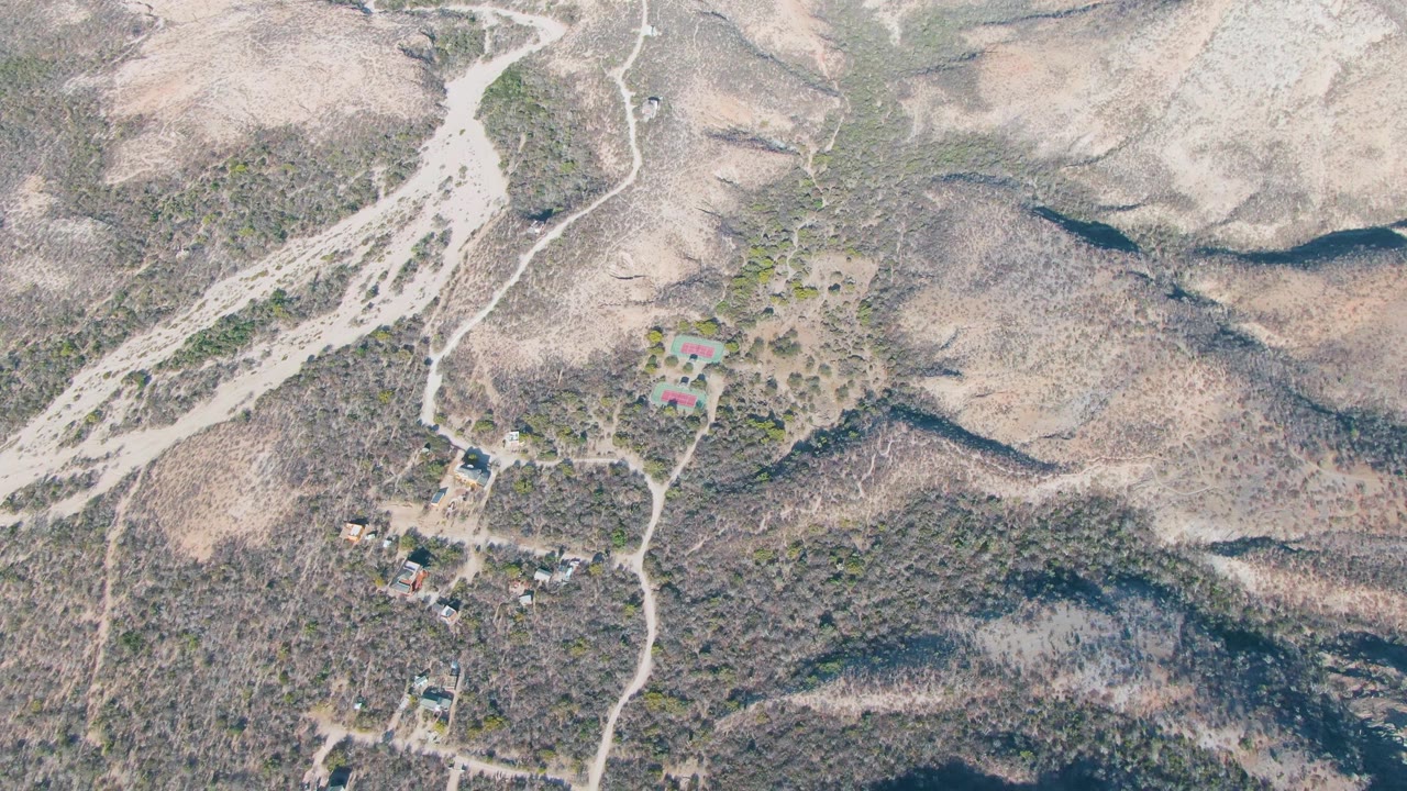 Aerial frame of dusty roads winding through sparse vegetation and hillside homes.