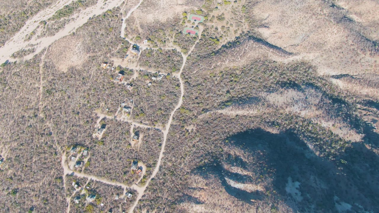 Aerial view in Cabo Pulmo, Baja California Sur, showing scrub-covered slopes, isolated buildings, branching dirt tracks, and no visible people.