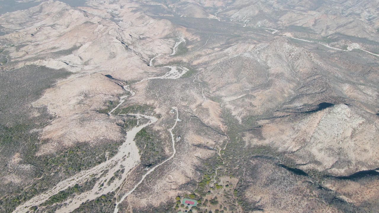 Aerial view over Cabo Pulmo arid mountain ridges with pale dirt roads, dry washes, scattered scrub, and no visible people.