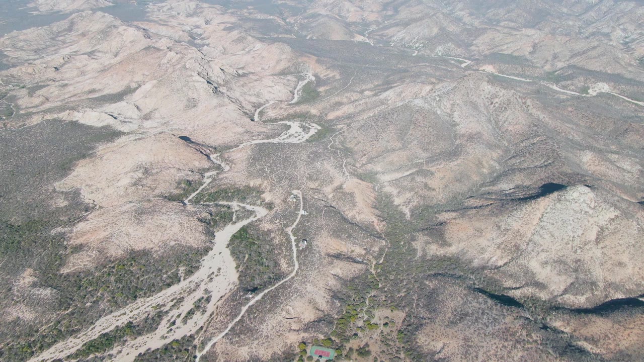 Cabo Pulmo aerial frame with tan and gray ridges, branching dry gullies, pale roads across the slopes, sparse shrubs, and no visible people.
