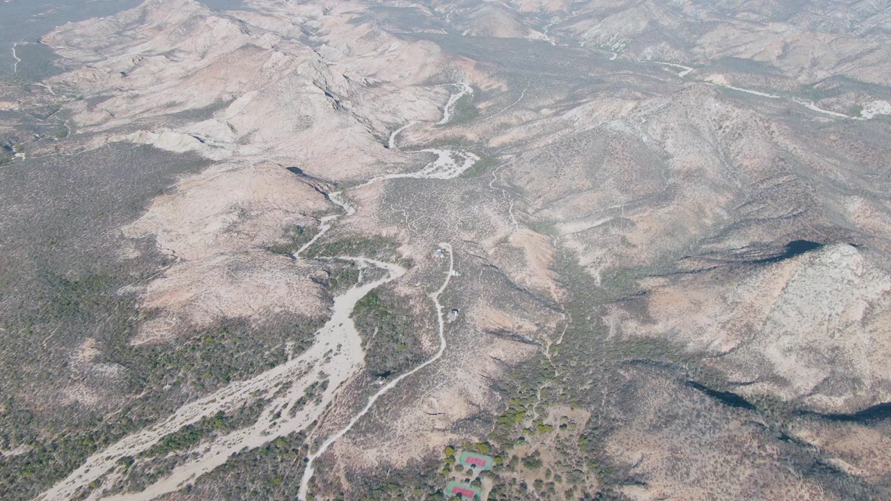 Aerial view of rocky arid hills and a pale winding wash