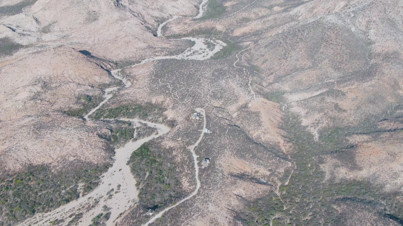 Aerial view in Cabo Pulmo, Baja California Sur with branching pale wash channels, gray-brown hills, scattered shrubs, and no visible people.