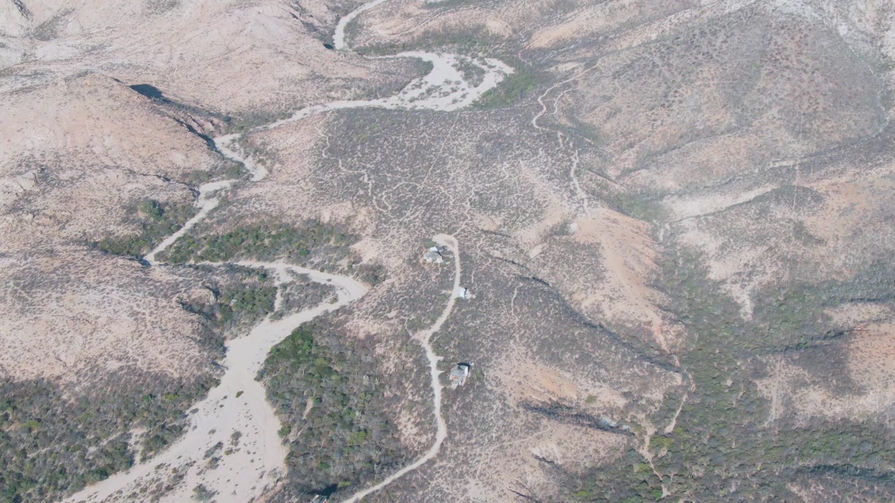 Aerial view of a winding dirt road through dry hills with a small vehicle