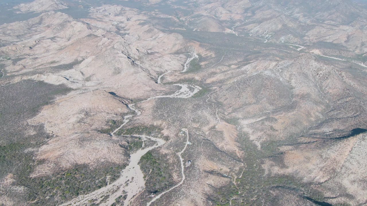 Aerial landscape of dry hills with a broad pale wash in the foreground.