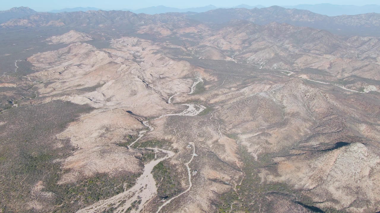 High aerial view across beige hills, scrubby terrain, and branching dry riverbeds.
