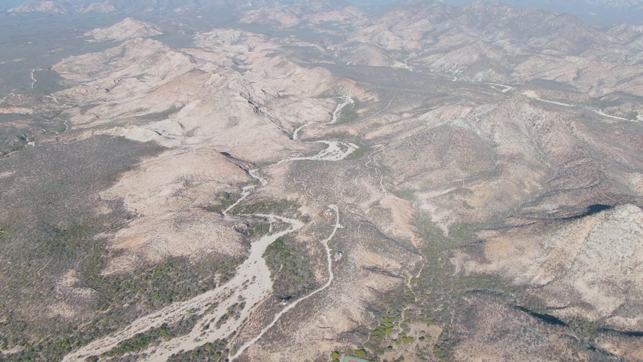 Aerial view of dry valley floor, rocky hills, and muted haze.