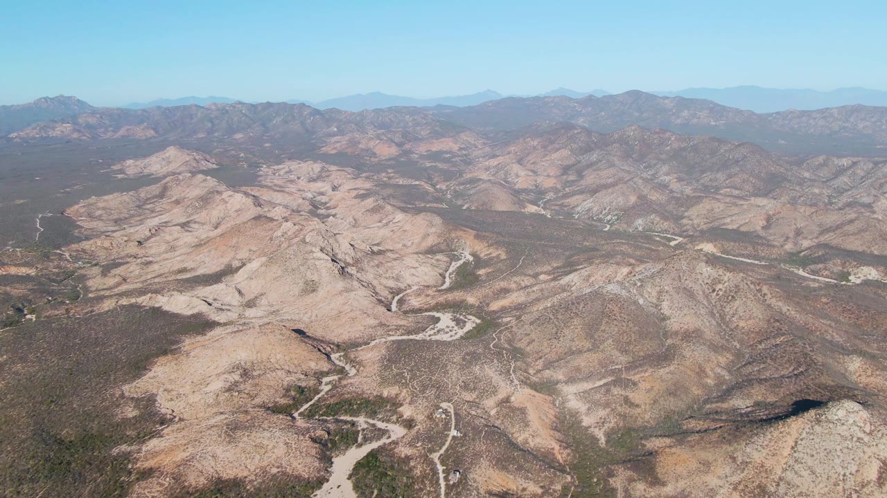 Wide aerial view of a dirt road curving through rocky desert hills.