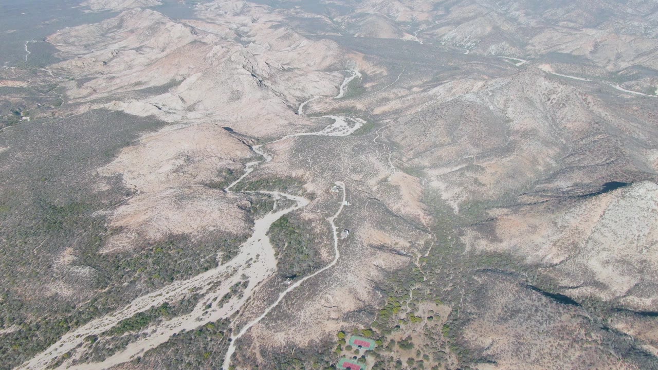 Aerial view across dry mountain slopes with pale riverbeds and dirt tracks.