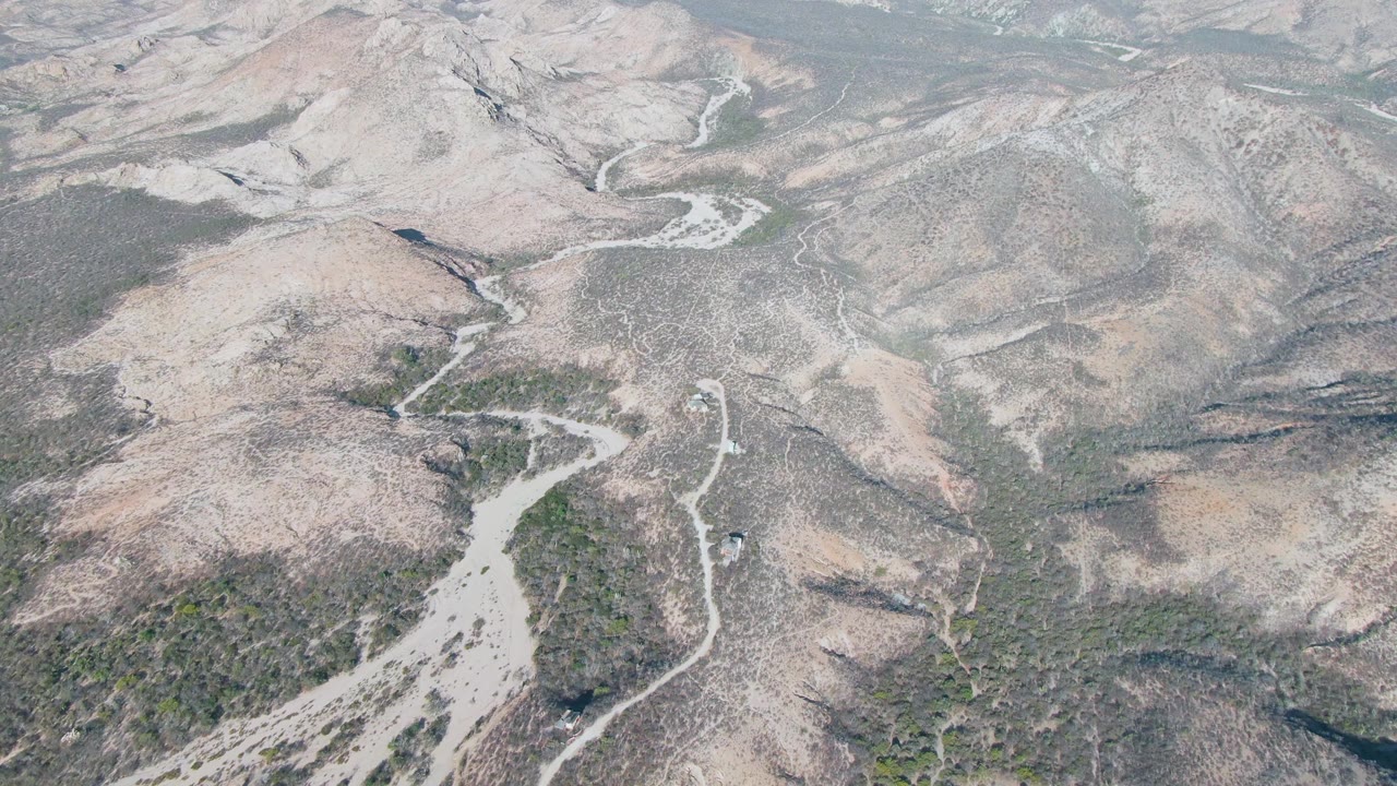 Aerial frame over Cabo Pulmo showing a pale dirt road cutting through rocky brown hills and sparse green vegetation, with no visible people.