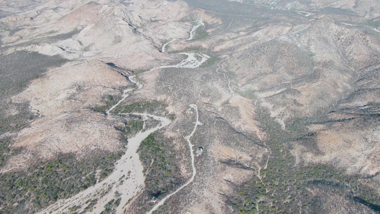 Drone view in Cabo Pulmo with a small vehicle on the winding dirt road, rocky slopes around it, and no visible people.