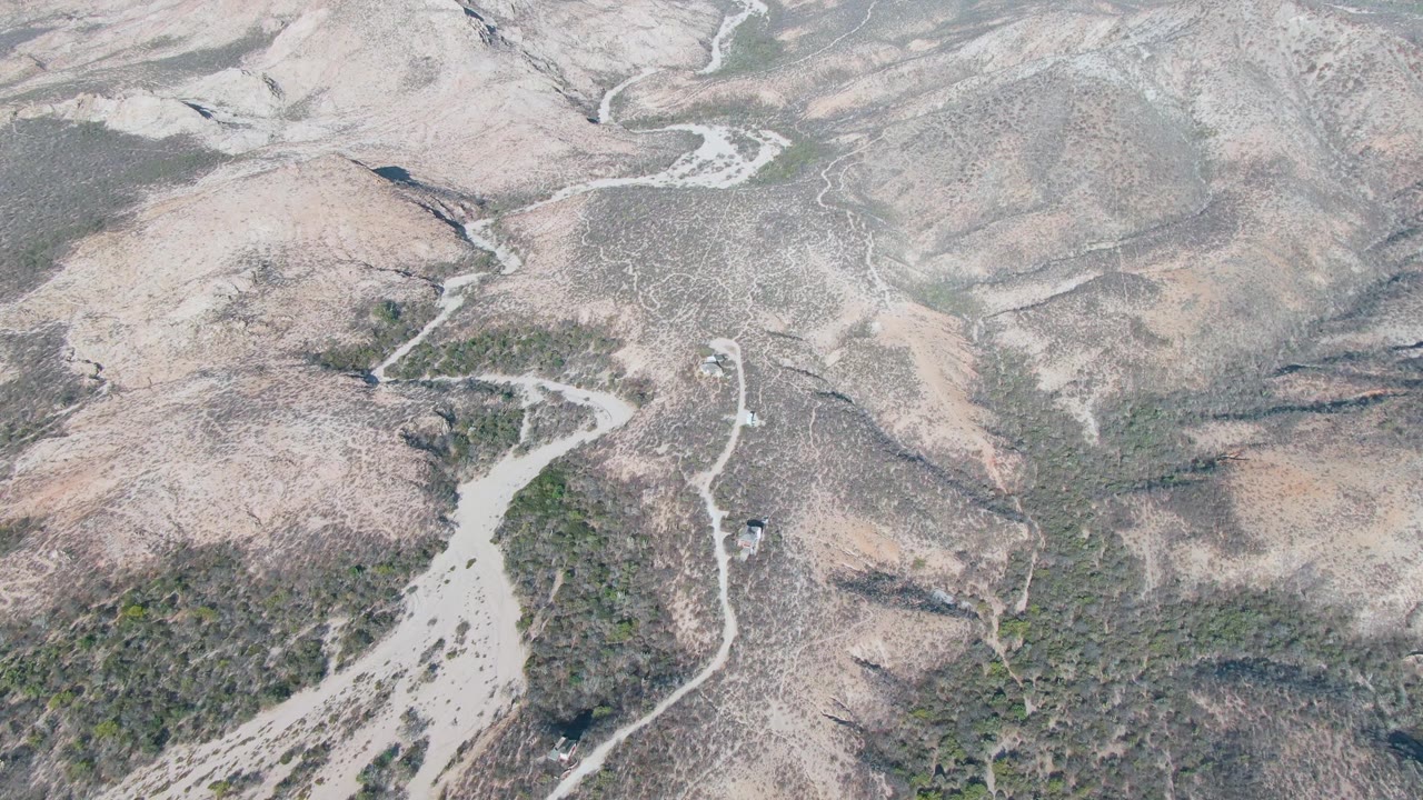 Aerial frame over Cabo Pulmo dry hills showing a pale dirt road crossing scrub-covered slopes with no visible people.