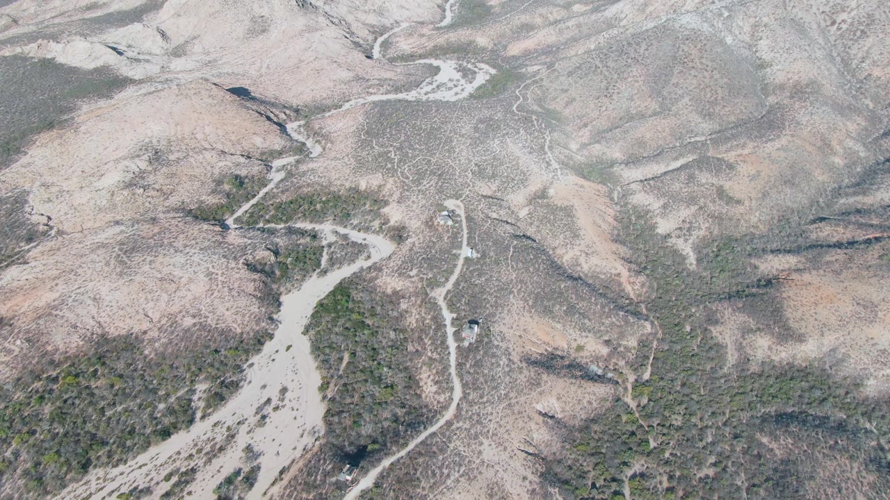 The road bends through Cabo Pulmo's dry hillside terrain, with scattered green shrubs and no visible people in the aerial view.