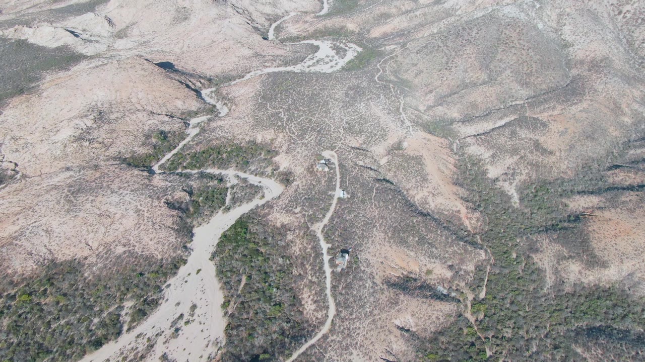 Aerial view of a vehicle on a winding dirt road in dry hills.