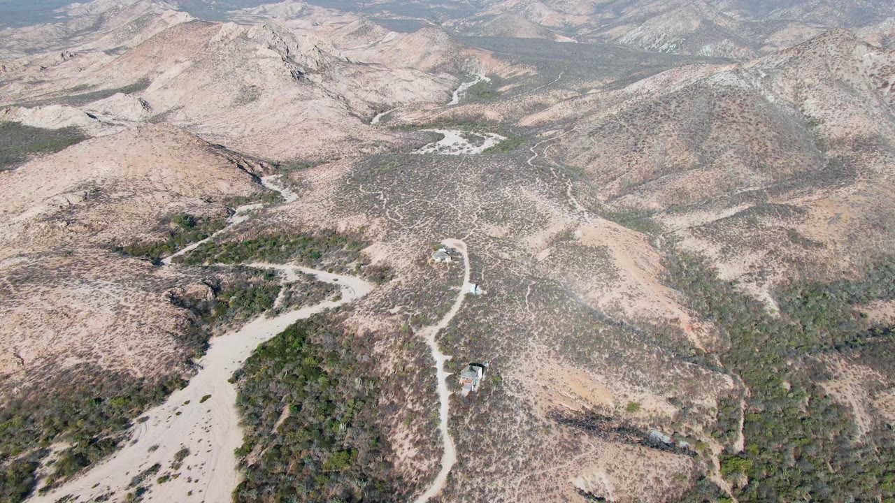 Aerial view of a winding dirt road through dry hills with a small vehicle.