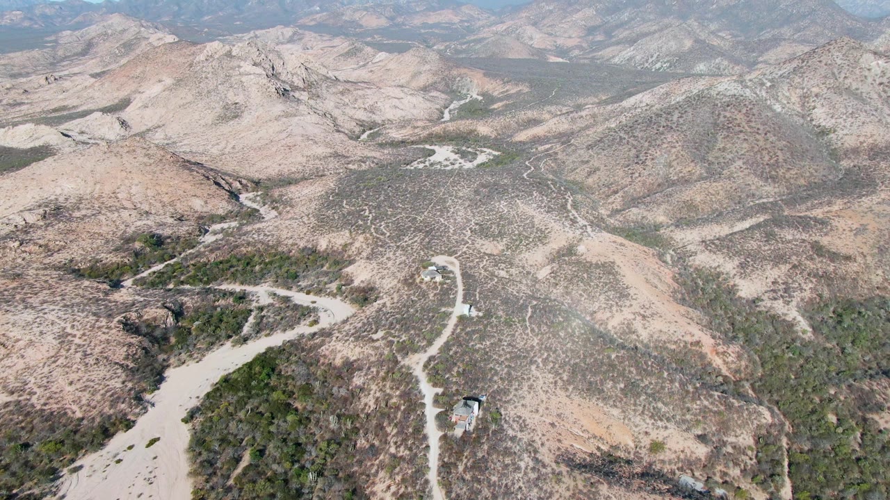 Aerial landscape of pale dry hills, scrub, and dirt roads under hazy sky
