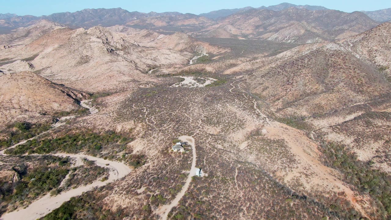 Drone view of desert hills with a winding road and distant ridges.