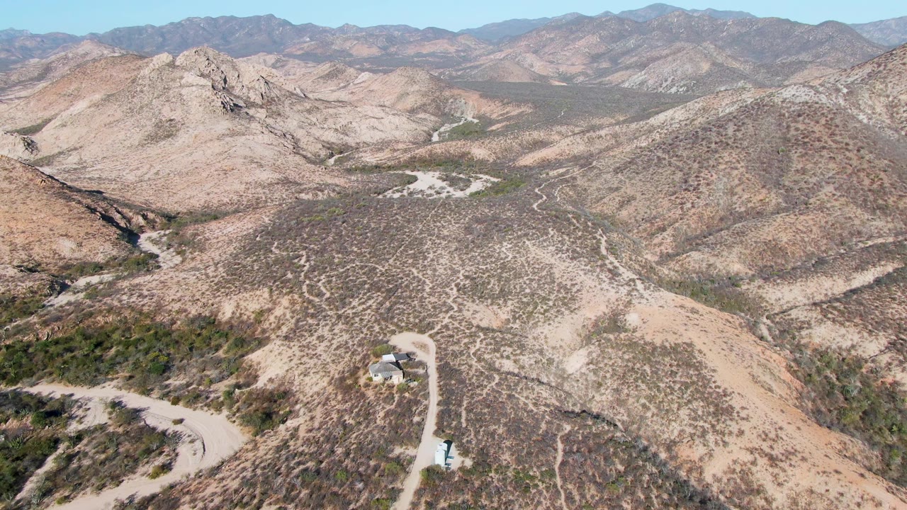 Dry mountain terrain with a curving dirt road and small structure below.