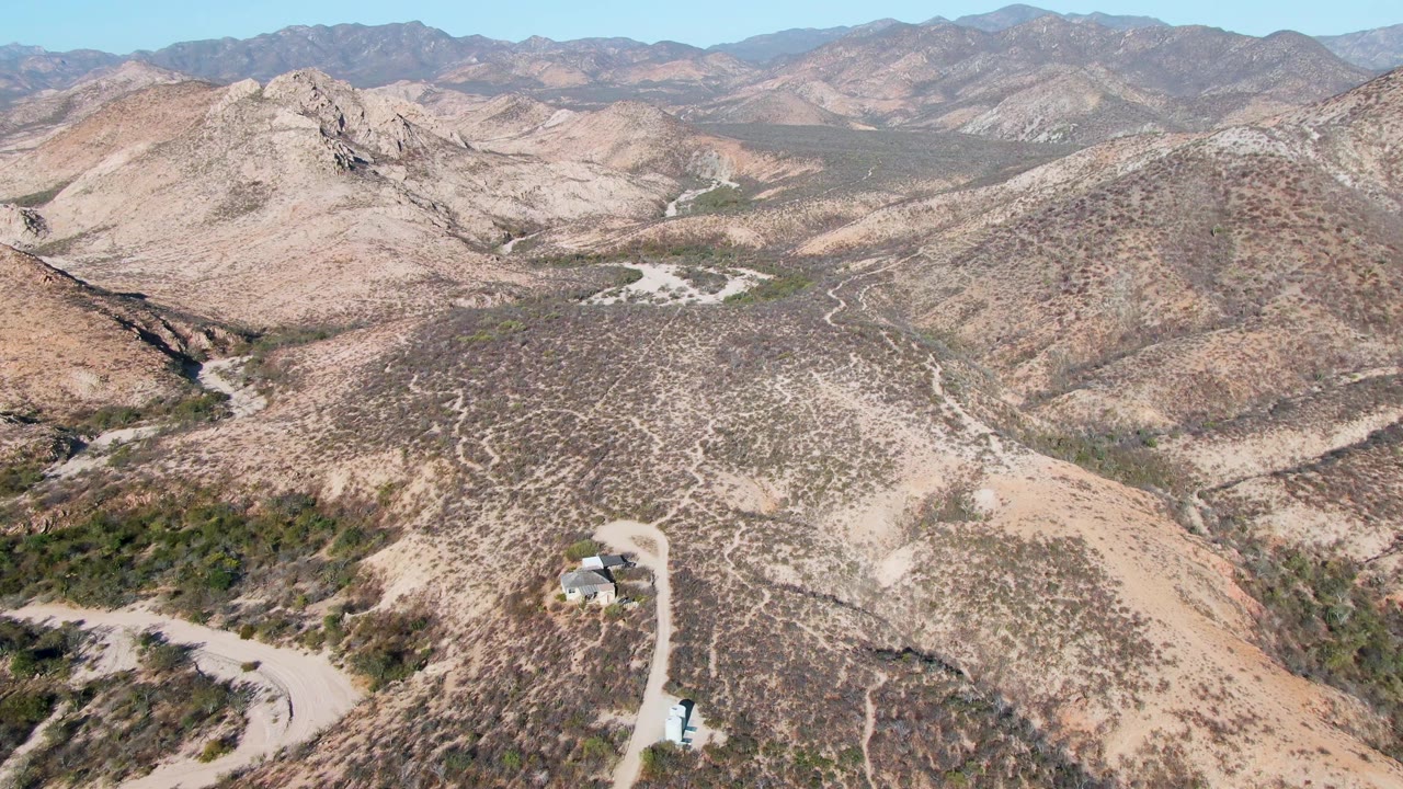 Cabo Pulmo desert hills fill the frame with a pale road bending through the lower slope, textured scrub patterns, distant ridges, and no visible people.