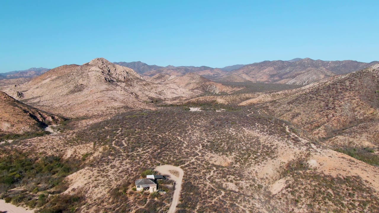 Dry mountain valley with a small hillside house and dirt road