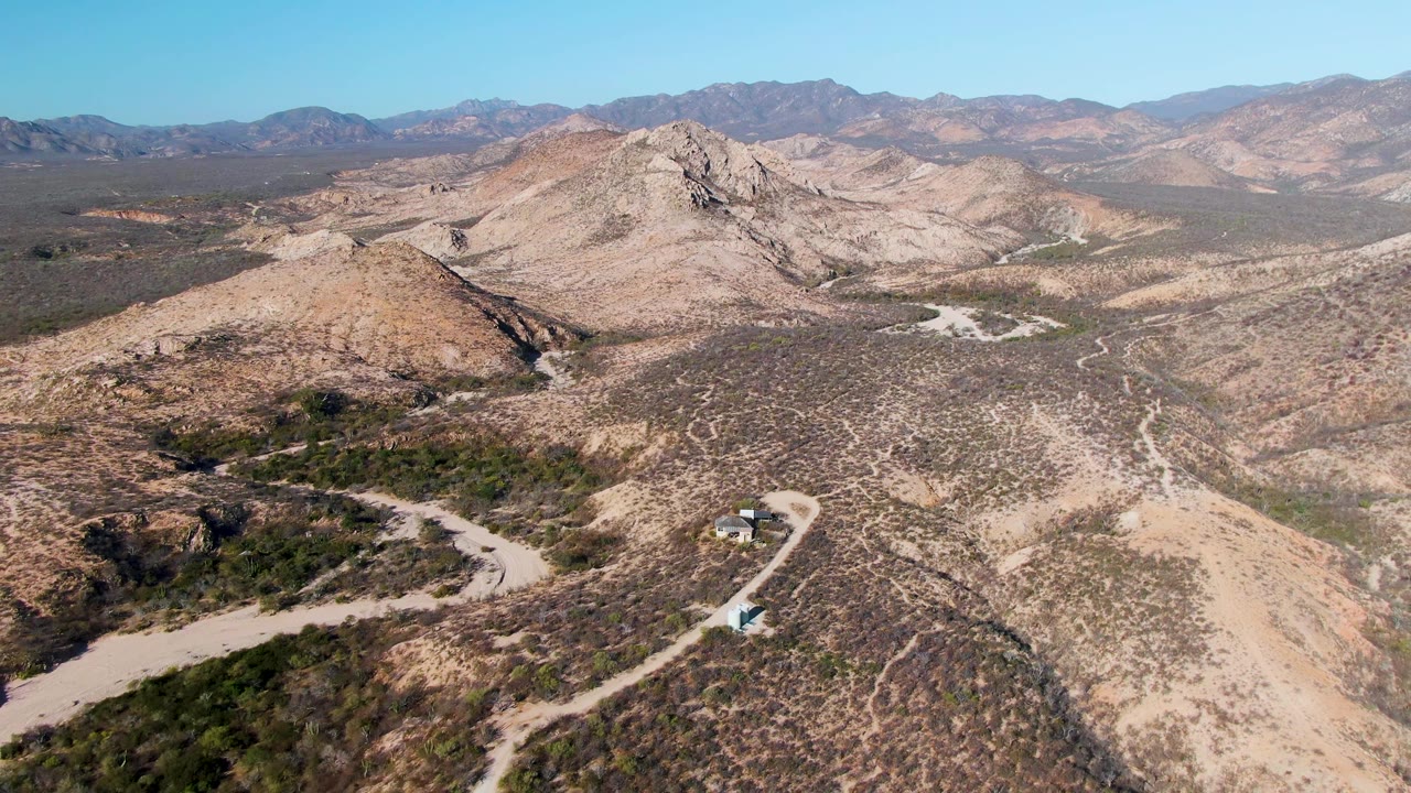 Drone view of tan desert ridges with a winding road below.