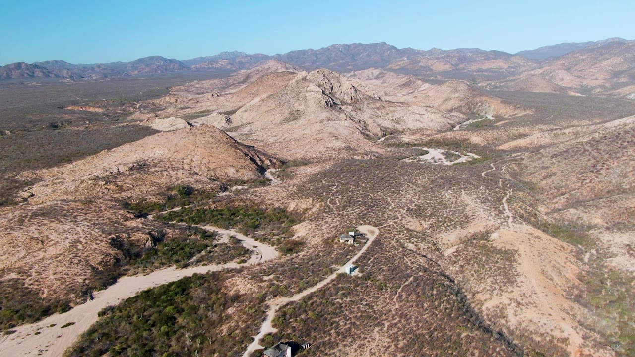 Aerial view of a vehicle on a winding dirt road through rocky desert hills.