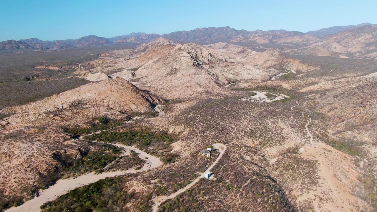 Small vehicle on a pale road through arid hills with mountains beyond.