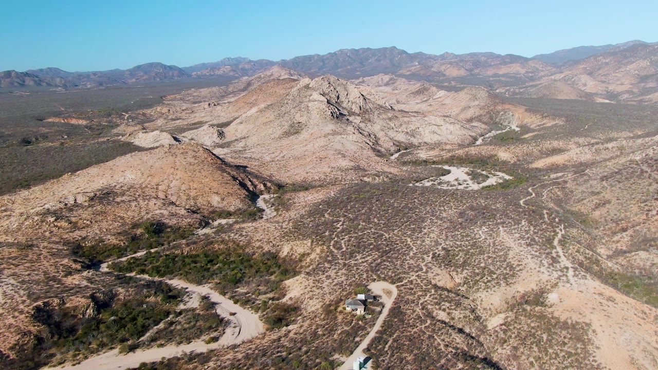 Drone view over a vehicle on a curved desert road below mountain ridges.