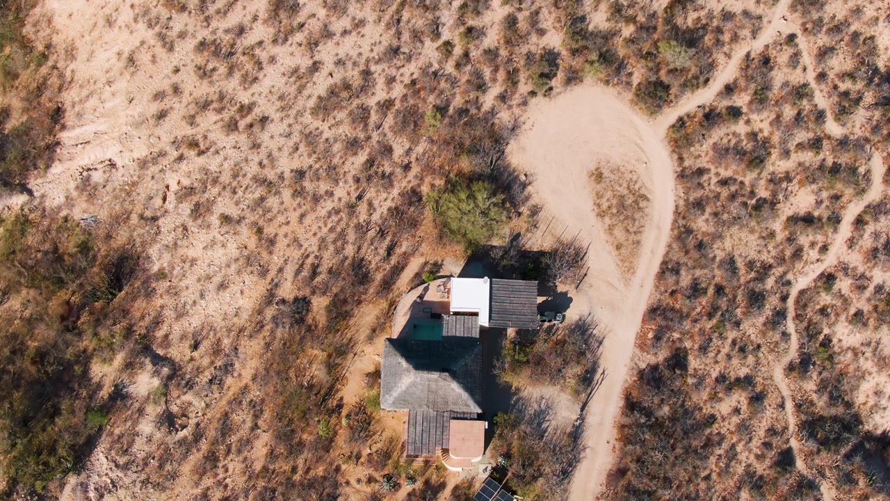Top-down desert house with dirt tracks through sparse vegetation.