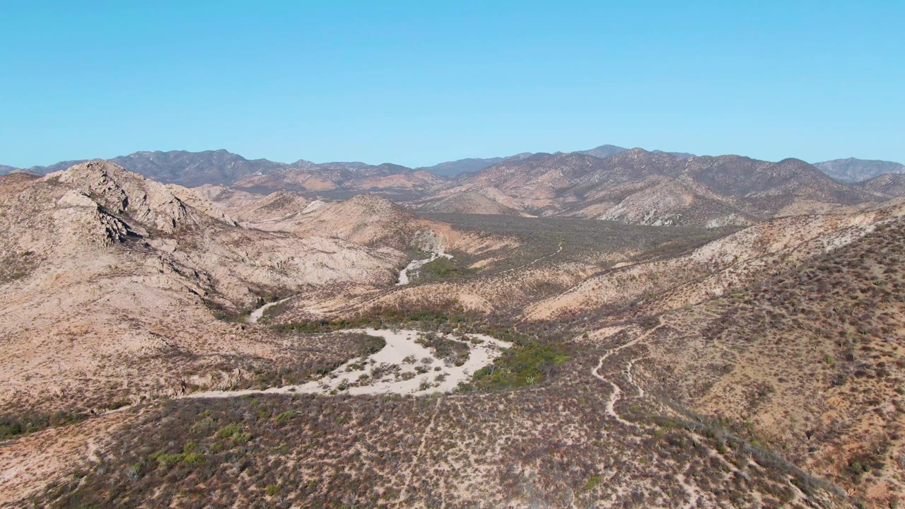 Aerial view of rocky desert hills and a winding pale dirt road under blue sky.