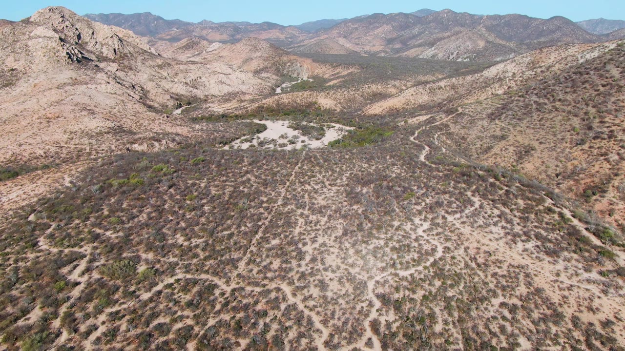 High aerial over arid hills and mountain backdrop