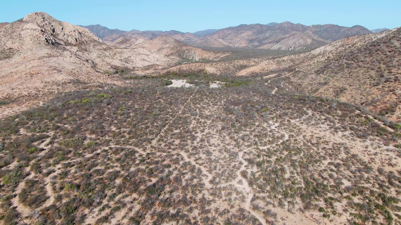 Aerial view of scrubby desert hills and distant mountains under blue sky.