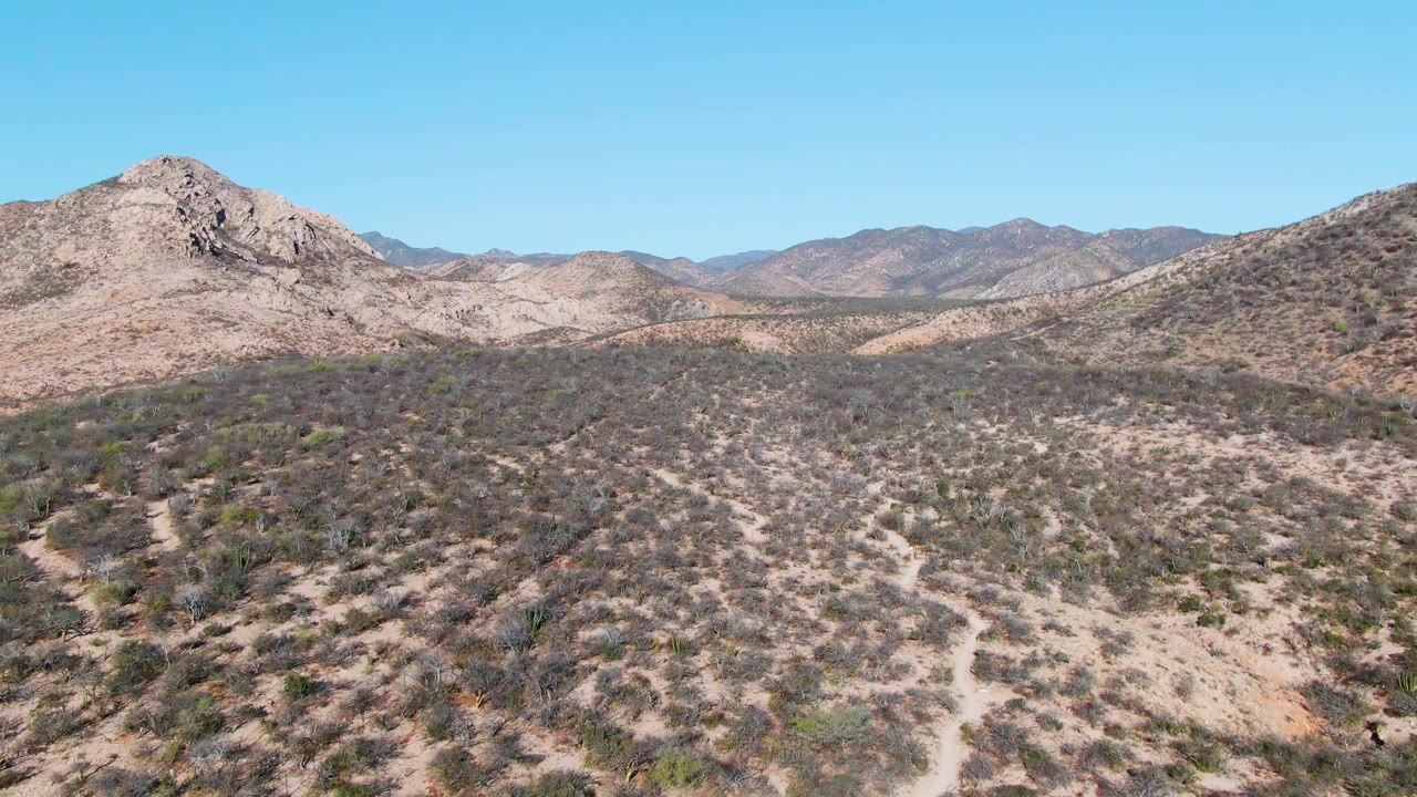 Aerial view of scrubby desert hills under a clear blue sky.