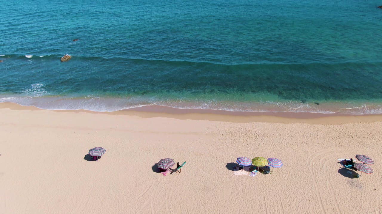 Top-down beach view with umbrellas, chairs, and a thin wave line.