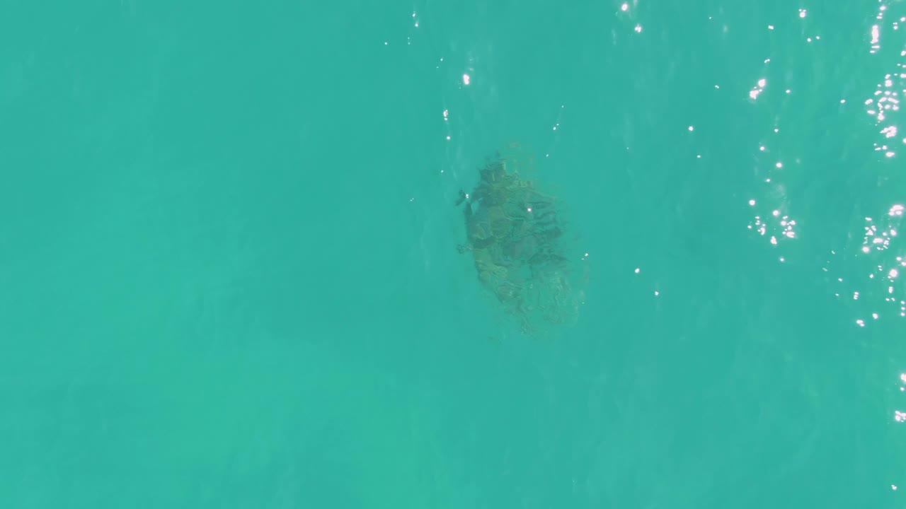 A dark coral formation sits below the turquoise surface in La Fortuna, with scattered white glints near the upper right and no visible people.