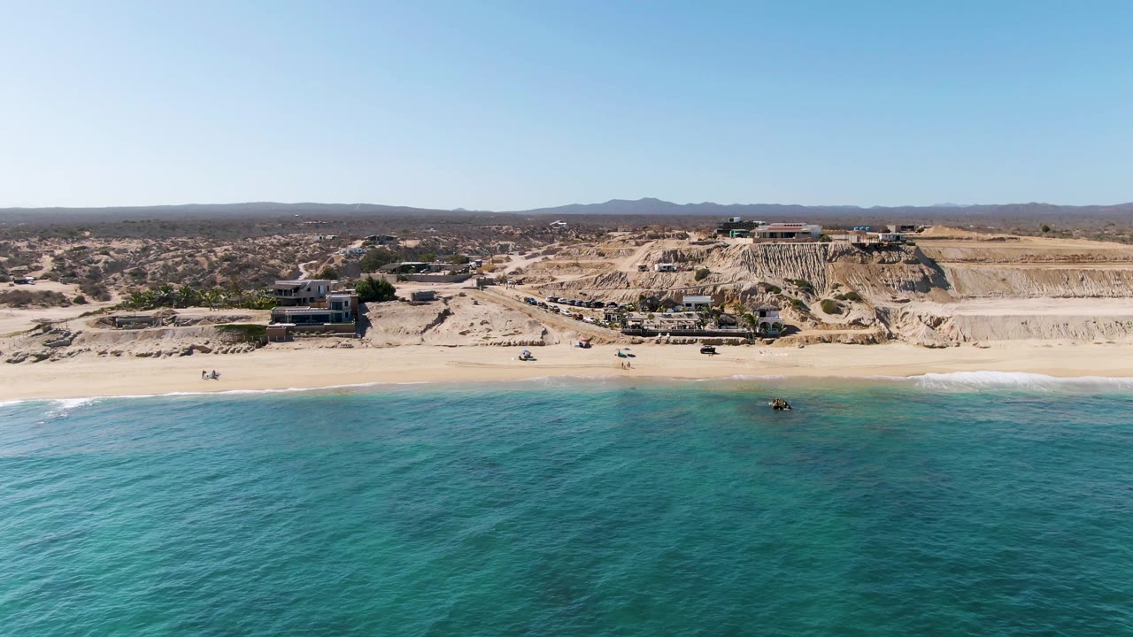 Aerial beach view with turquoise water and cliffside buildings behind the sand.