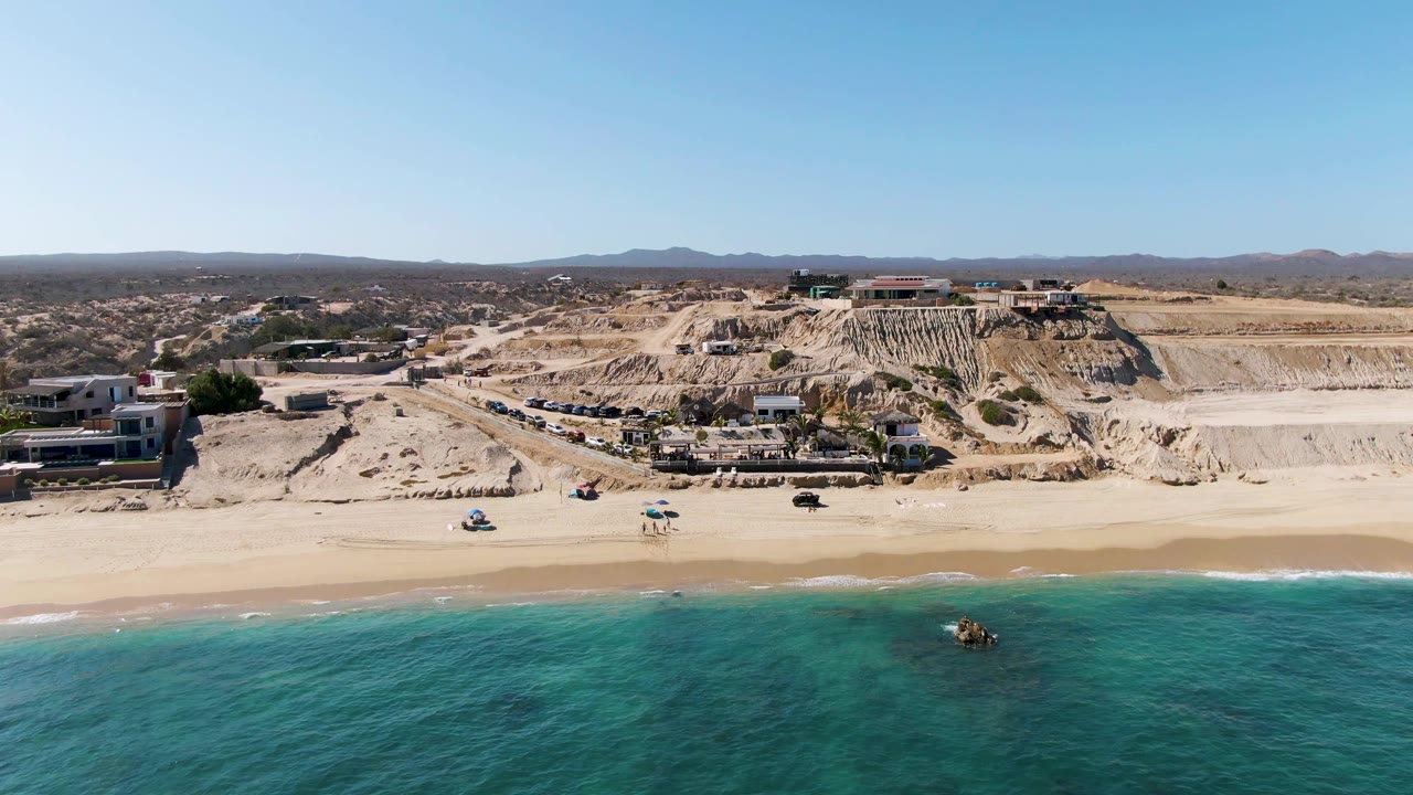 Aerial beach view with golf cart on sand and cliffside buildings behind