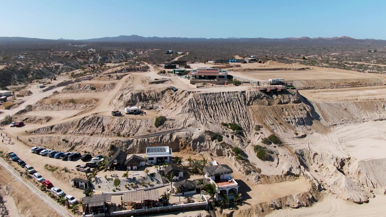 Aerial frame of quarry terraces, parked cars, small structures, and open desert.