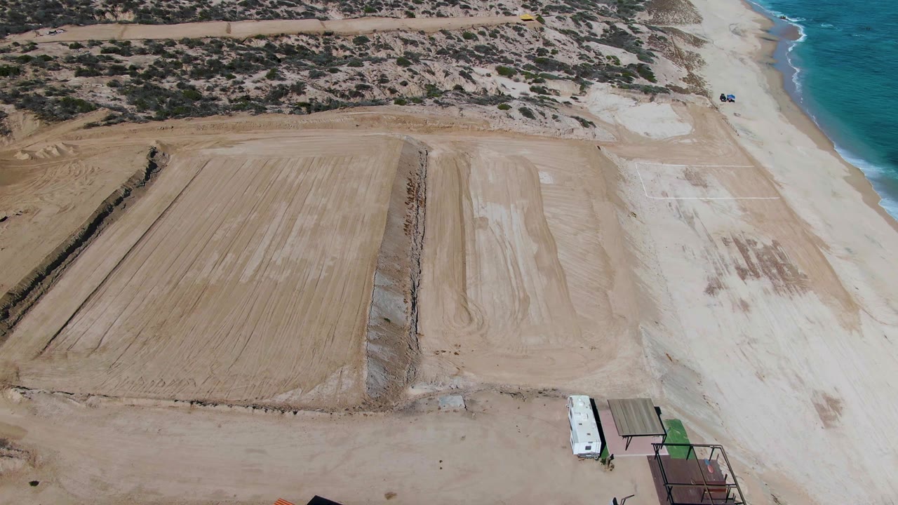 Drone view of sand grading area with a white vehicle near the shore.